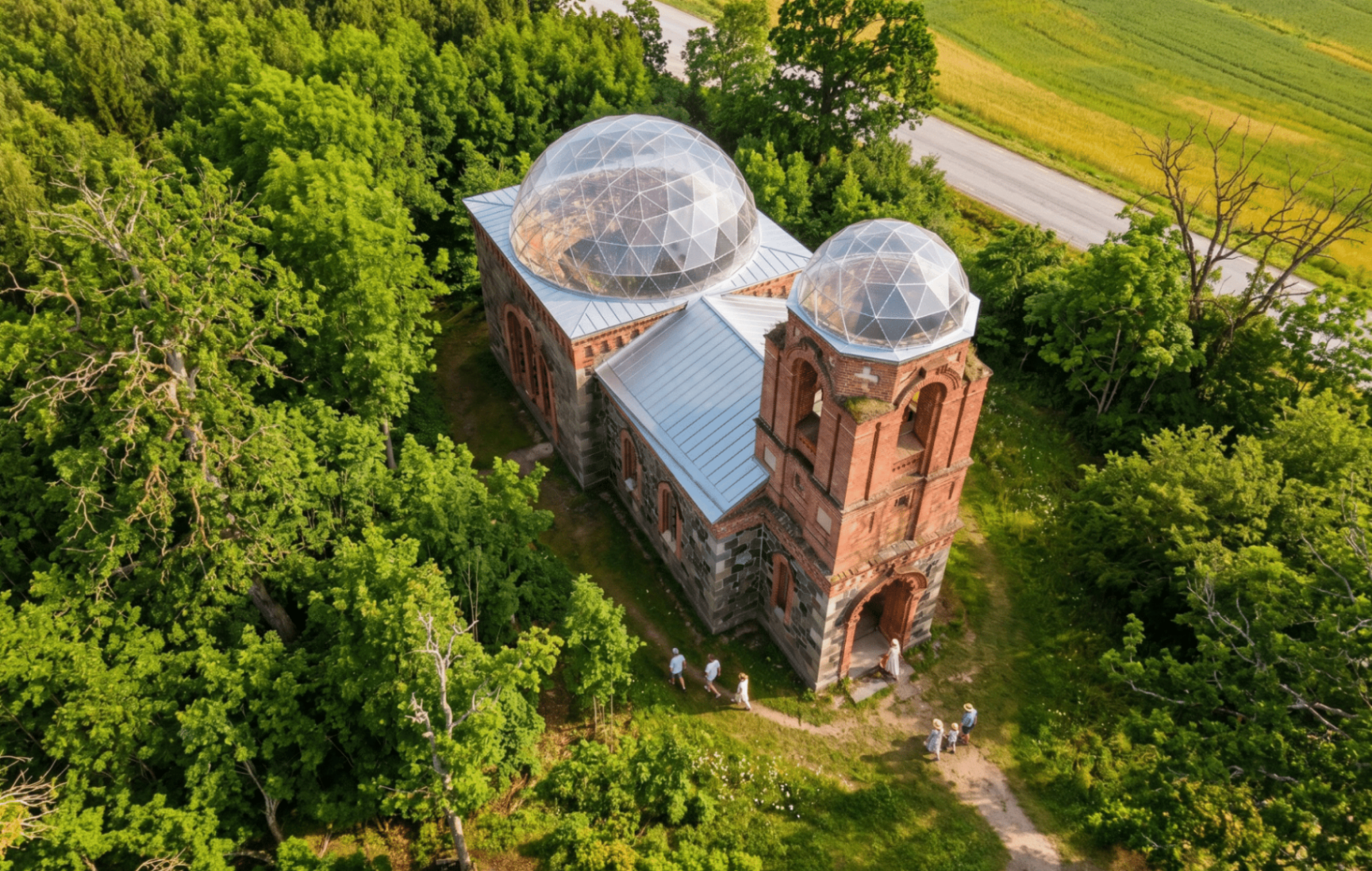 Kevadine droonifoto Sinalepa kirikust — kaks geodeetilist klaaskuplit rohelusse mattunud metsamaastiku keskel